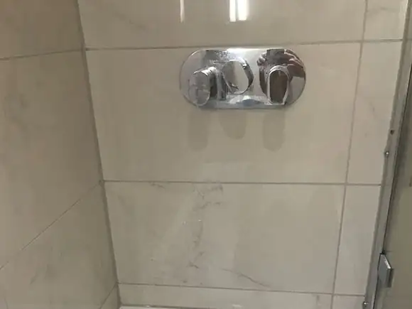 Stone shower wall with chrome controls and horizontal tile joints