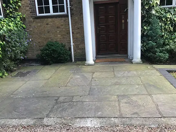 Stone entrance paving before restoration, darkened and patched with green organic staining