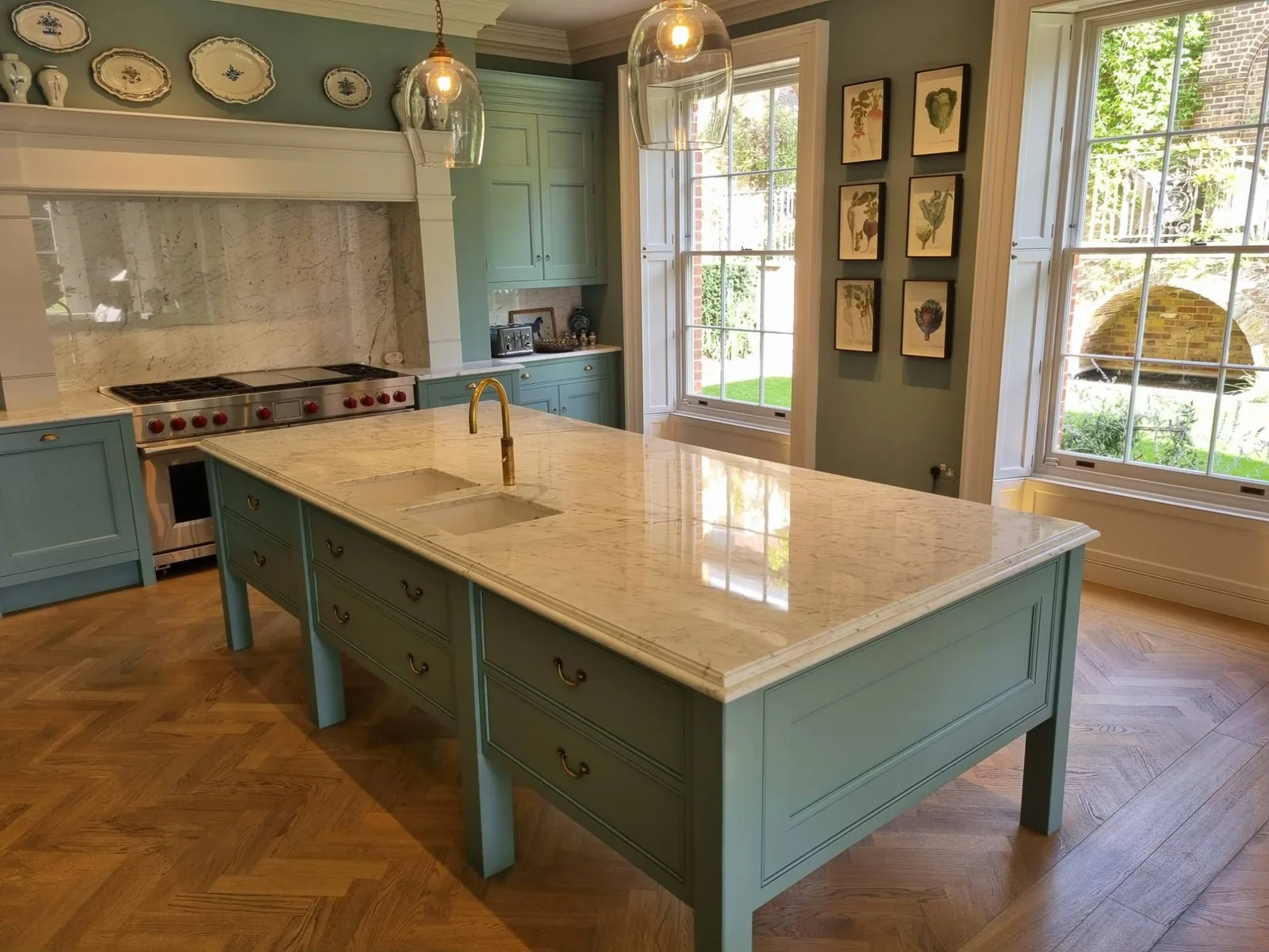 Veined marble island worktop with twin sinks and a brass tap, on green painted cabinetry