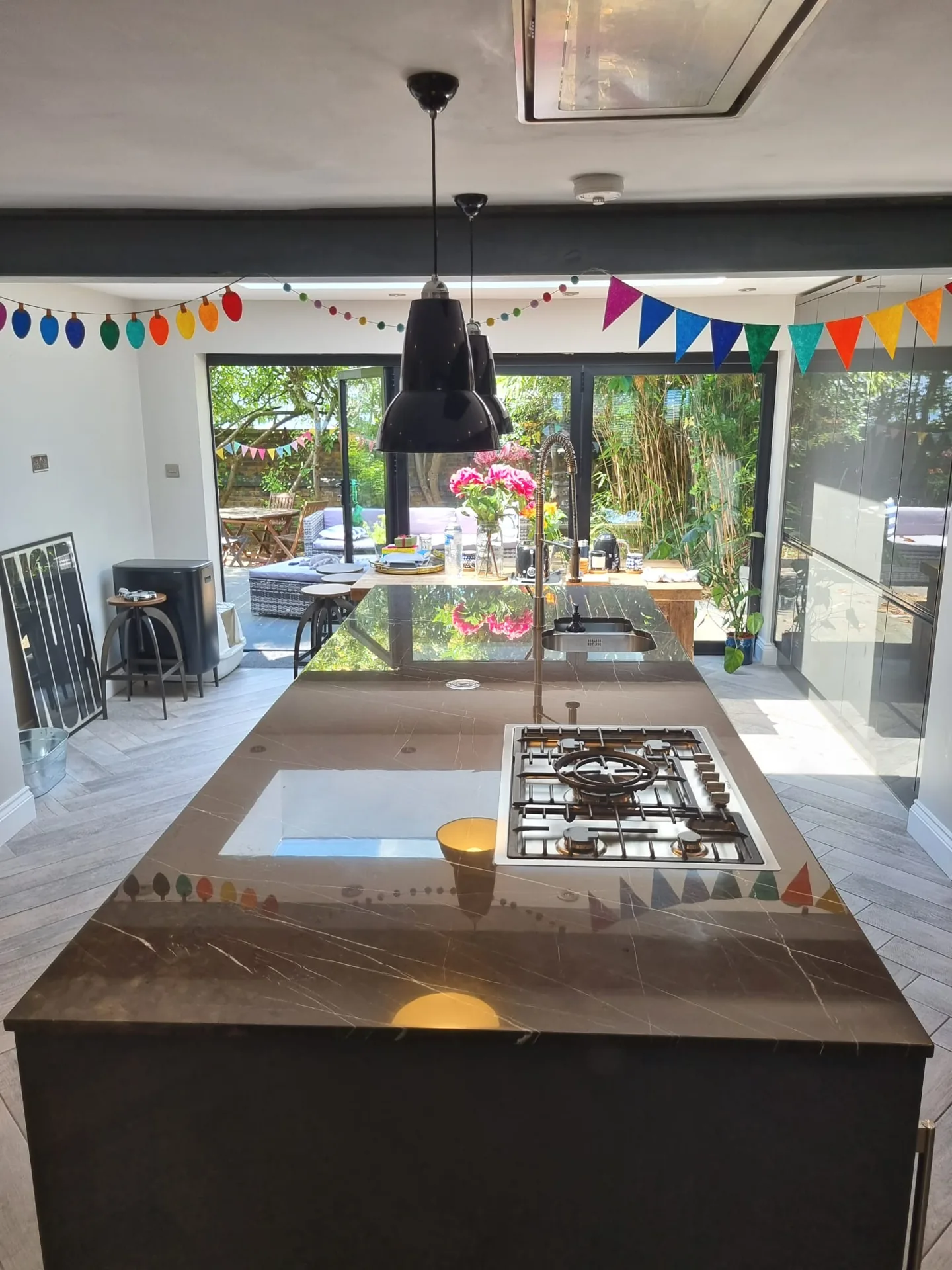 Dark kitchen island with an inset hob, seen towards glazed doors