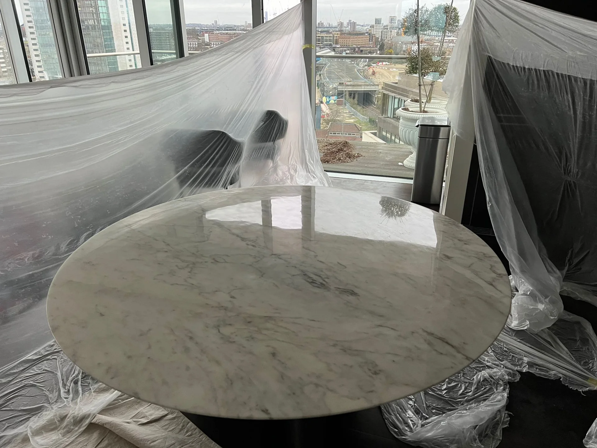 Round veined stone table beside glazing, with protective sheeting around the work area